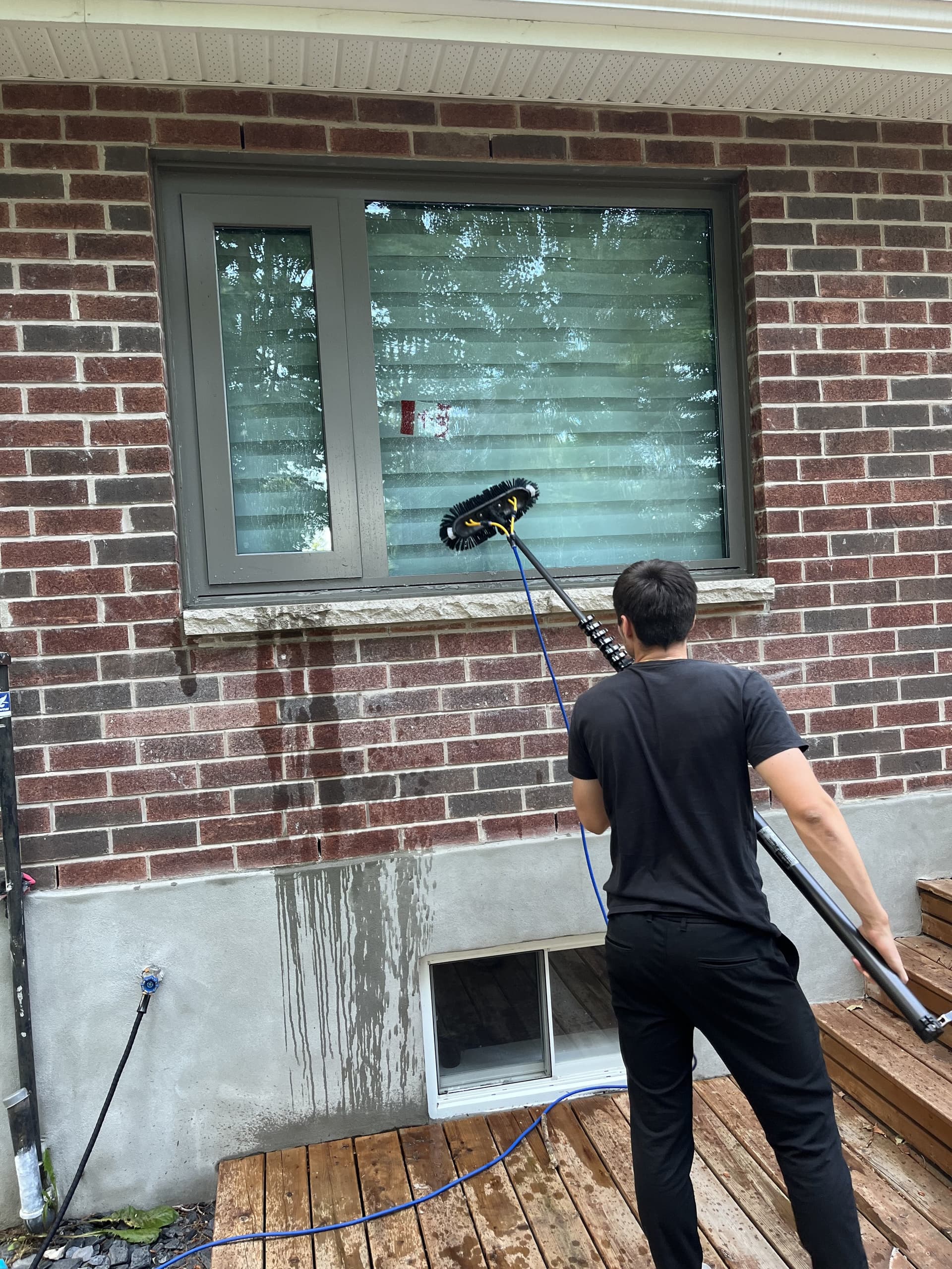 Team member cleaning a window with a water-fed pole on a brick house exterior