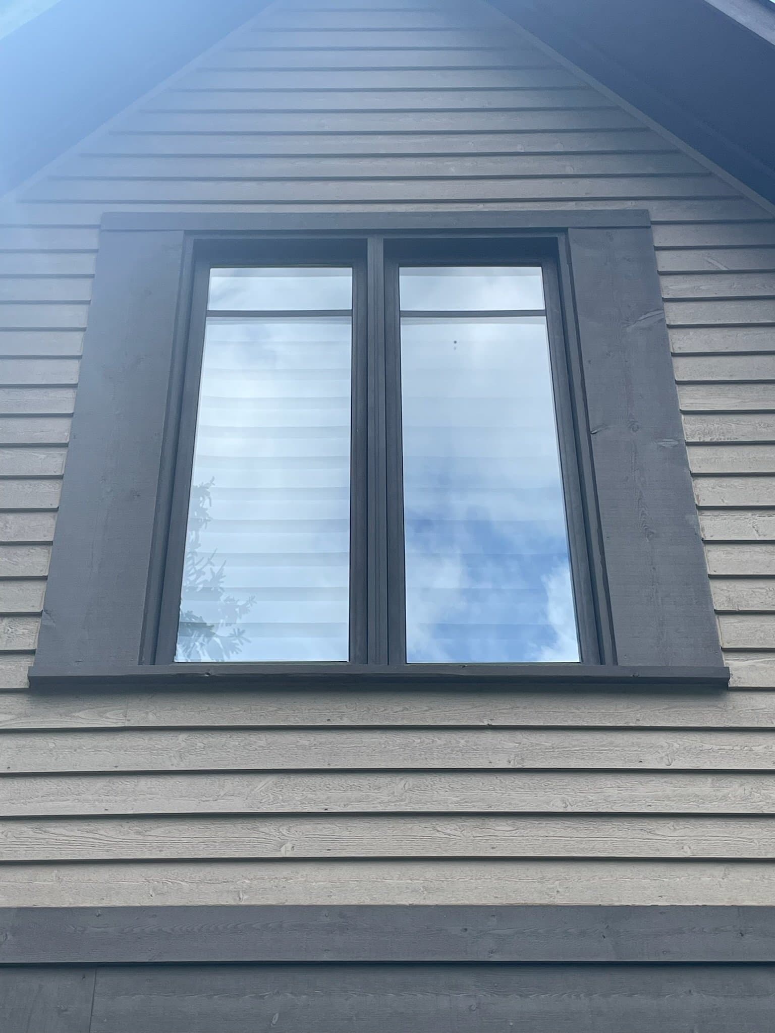 Double-pane window reflecting blue sky and clouds on a gray-sided house